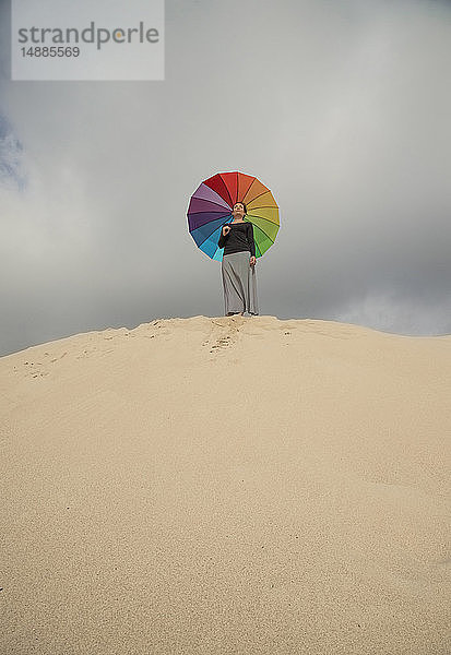 Frau mit buntem Regenschirm auf einer Düne stehend