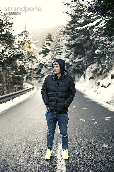 Junger Mann steht auf einer verschneiten Straße mit Bäumen im Hintergrund