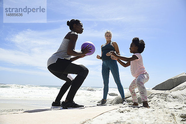 Mutter mit Tochter und Freund trainieren mit einem Ball am Strand