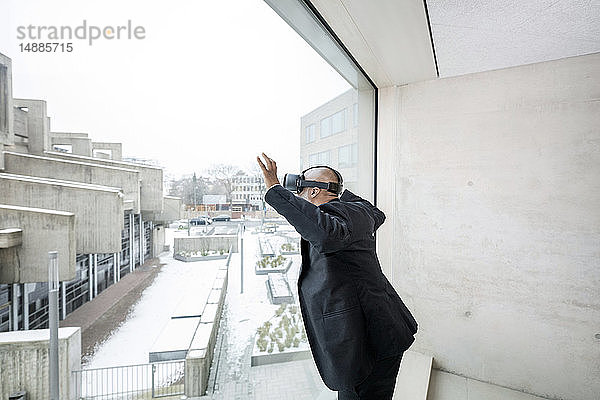 Reifer Geschäftsmann mit einer Virtual-Reality-Brille  die aus dem Fenster schaut