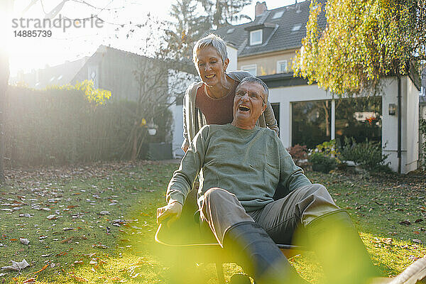 Glückliches älteres Ehepaar vergnügt sich mit Schubkarre im Garten