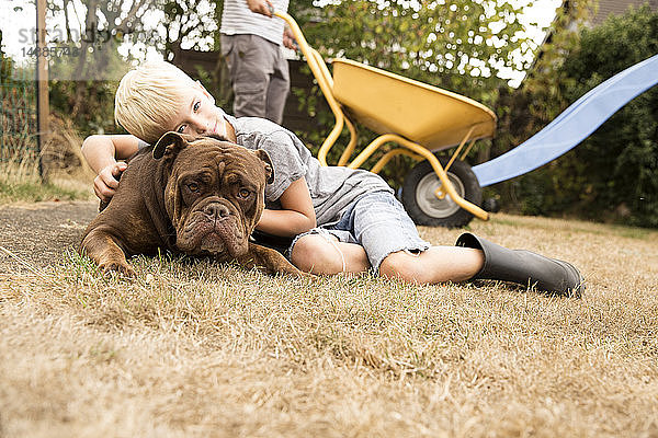 Junge kuschelt mit Old English Bulldog auf Spielplatz im Garten