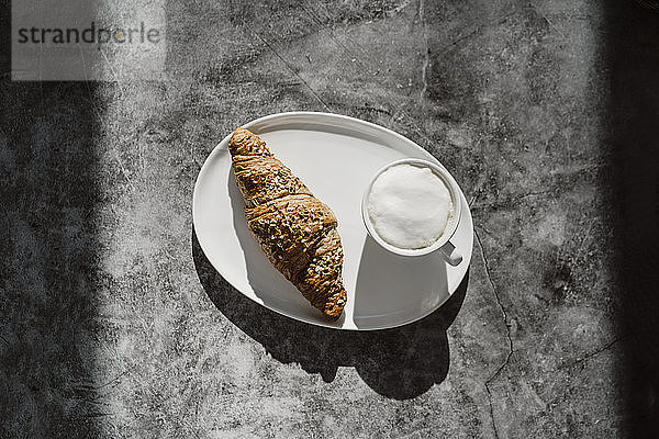 Tasse weisser Kaffee und ein Croissant für die ganze Mahlzeit auf dem Teller