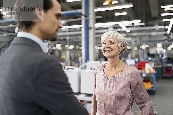 Lächelnde ältere Geschäftsfrau und Geschäftsmann im Gespräch in einer Fabrik