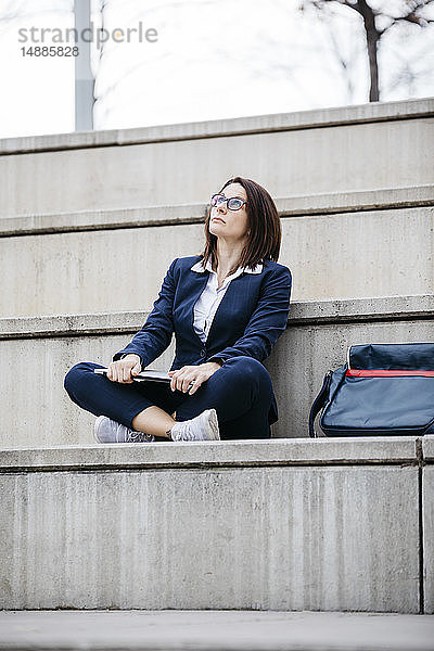 Geschäftsfrau sitzt im Freien auf einer Treppe mit Laptop und schaut nach oben