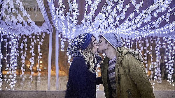 Junges Paar küsst sich in winterlicher Dekoration