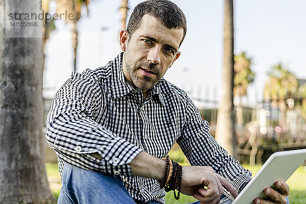 Porträt eines im Stadtpark sitzenden Mannes mit digitalem Tablett