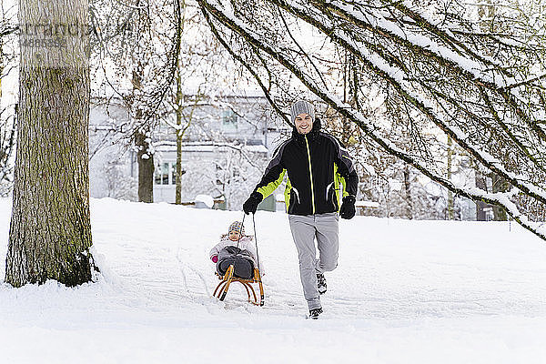 Glücklicher Vater mit Tochter auf Schlitten in Winterlandschaft