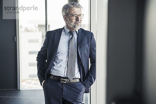 Lächelnder reifer Manager schaut im Büro aus dem Fenster