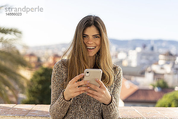 Porträt einer lachenden jungen Frau mit Handy in der Hand