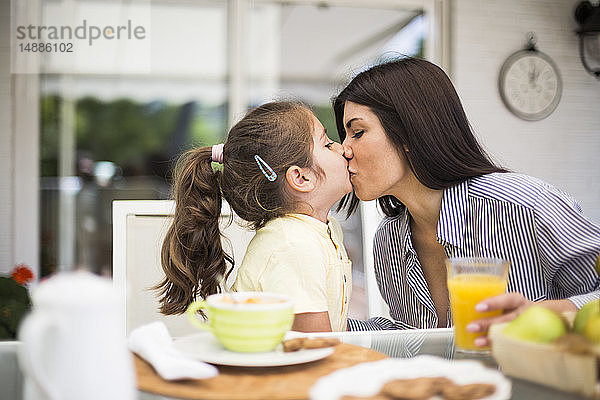 Mutter und Tochter küssen sich beim Frühstück zu Hause