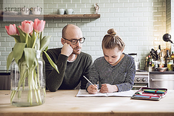 Vater und Tochter sitzen in der Küche und machen Hausaufgaben