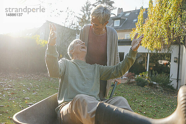 Glückliches älteres Ehepaar vergnügt sich mit Schubkarre im Garten