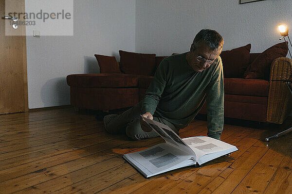 Älterer Mann sitzt zu Hause auf dem Boden und schaut sich ein Fotoalbum an