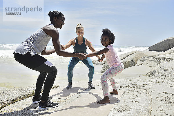 Mutter mit Tochter und Freundin bei einer Fitnessübung am Strand