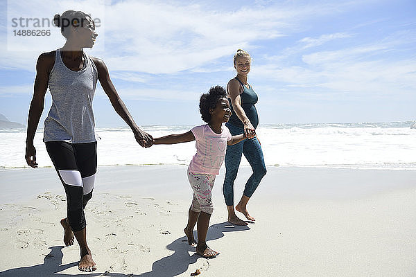 Glückliche Mutter mit Tochter und Freundin am Strand spazieren