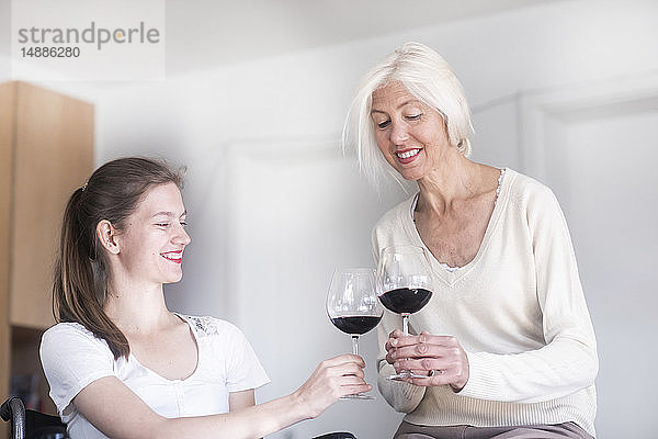 Mutter und Tochter im Rollstuhl bei einem Glas Rotwein zu Hause