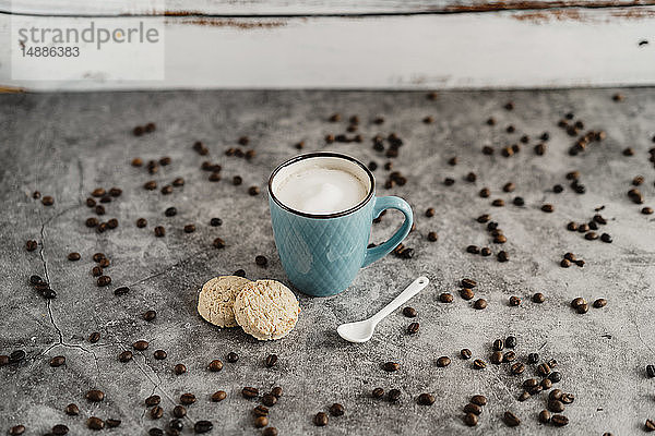 Tasse weißer Kaffee  Vollkornplätzchen  Porzellanlöffel und verstreute Kaffeebohnen