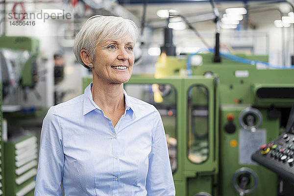 Porträt einer lächelnden älteren Geschäftsfrau in einer Fabrik  die sich umsieht