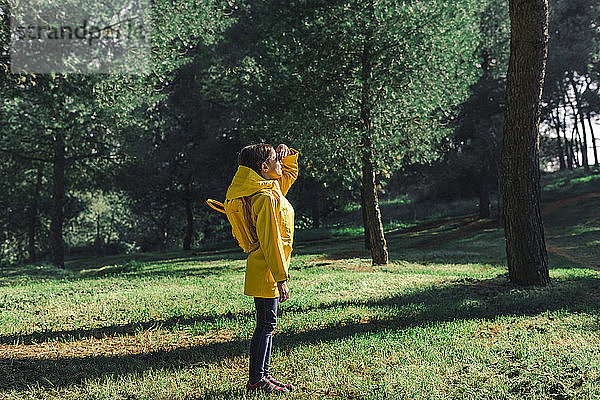 Mädchen in gelbem Regenmantel und gelbem Rucksack steht auf einer Wiese im Sonnenlicht