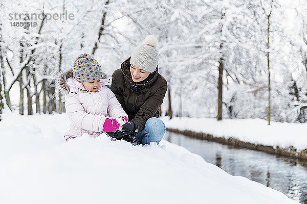 Glückliche Mutter mit Tochter an einem Wassergraben in Winterlandschaft