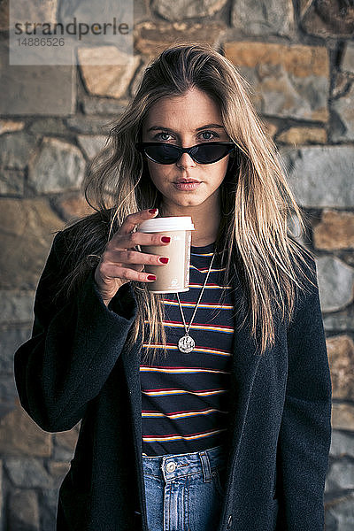 Porträt einer jungen Frau mit Sonnenbrille und Kaffee zum Mitnehmen