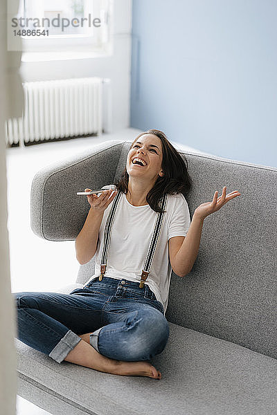 Hübsche Frau sitzt auf der Couch  benutzt ein Smartphone und lacht
