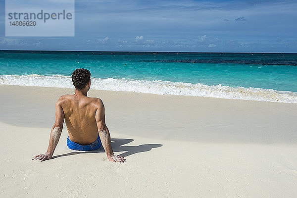Karibik  Anguilla  Mann am Strand sitzend  Rückansicht
