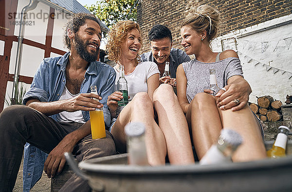 Freunde entspannen sich im Sommer in einem Hinterhof  junge Frauen kühlen ihre Füße in einer Wanne mit Getränken