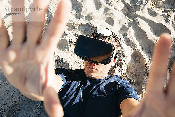 Mann mit VR-Brille liegt im Sand am Strand