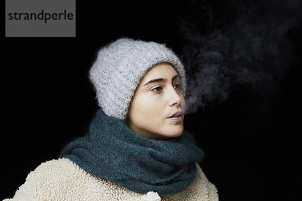 Porträt einer jungen Frau in Winterkleidung beim Rauchen