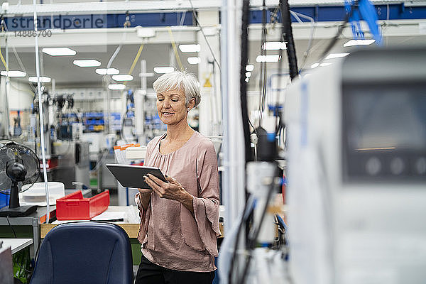 Lächelnde ältere Frau mit Tablette in einer Fabrik