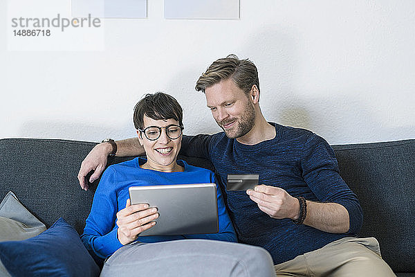 Glückliches Paar entspannt auf der Couch mit Tablette und Kreditkarte