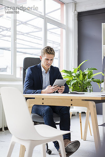 Selbstbewusster junger Geschäftsmann sitzt am Schreibtisch im Büro mit Tablett