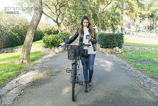 Junge Frau mit Fahrrad im Park mit Mobiltelefon