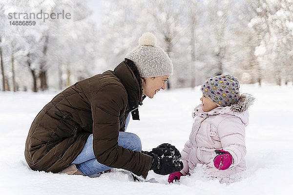Glückliche Mutter spielt mit Tochter in Winterlandschaft