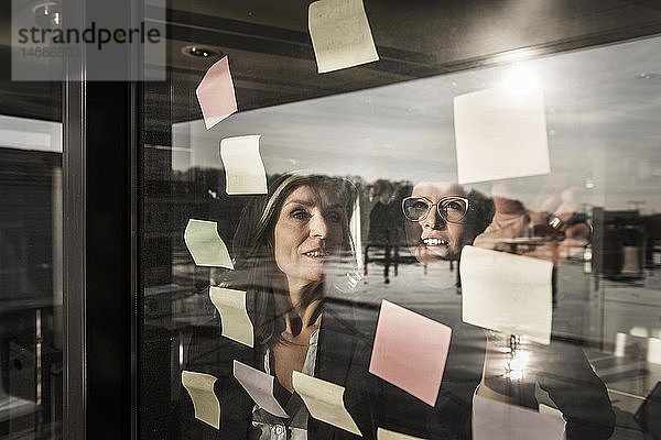 Zwei Geschäftsfrauen machen ein Brainstorming und kleben Haftnotizen an die Fensterscheibe