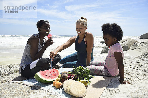 Mutter mit Tochter und Freundin beim Picknick am Strand