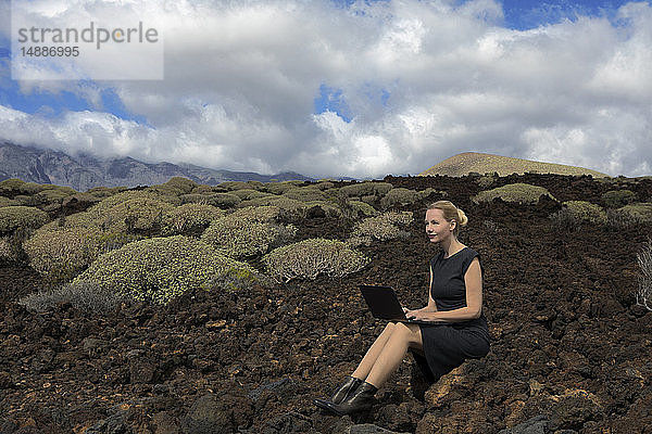 Spanien  Teneriffa  Malpais de Guimar  Frau sitzt in Vulkanlandschaft mit Kakteen am Laptop