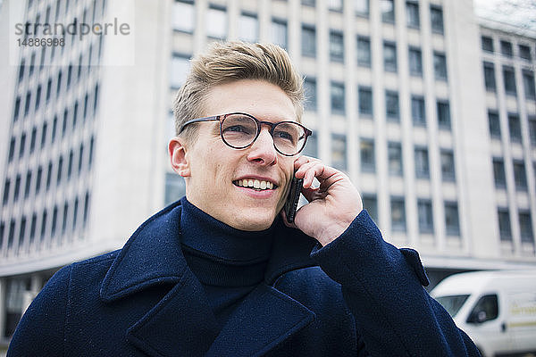 Porträt eines lächelnden jungen Mannes beim Telefonieren in der Stadt
