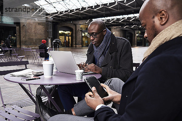 Zwei Geschäftsleute sitzen am Tisch eines Cafés und benutzen mobile Geräte