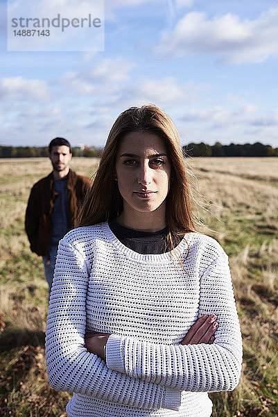 Junge Frau steht mit einem Mann hinter ihr auf einem Feld