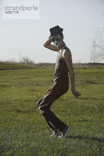 Porträt eines jungen Mannes mit weißer Gesichtsbemalung  der auf einer Wiese tanzt