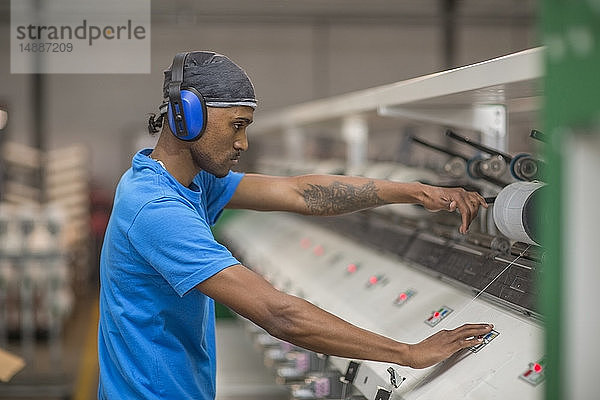 Mann trägt Gehörschützer bei der Bedienung einer Maschine in einer Fabrik