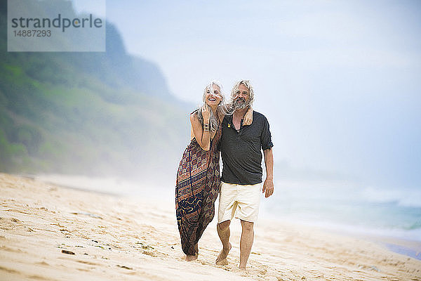 Glückliches älteres Hippie-Paar schlendert Seite an Seite am Strand