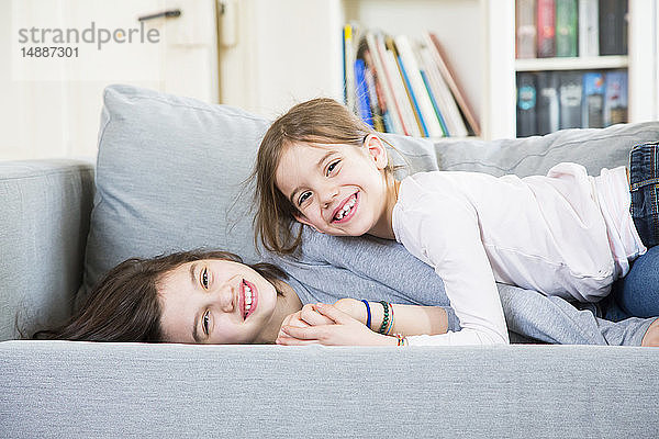 Porträt von zwei glücklichen Schwestern  die auf der Couch kuscheln