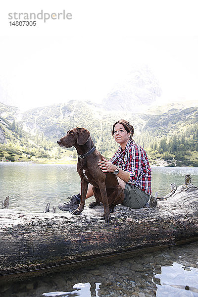 Österreich  Tirol  Frau mit Hund auf Baumstamm sitzend am Seebensee