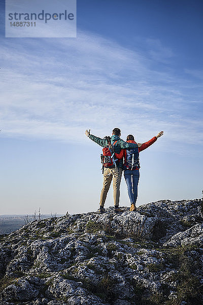 Glückliches Paar auf einer Wanderung in den Bergen auf einem Felsen stehend und die Aussicht genießend
