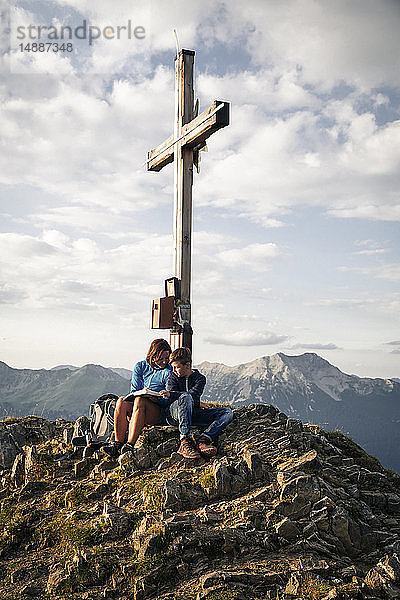 Österreich  Tirol  Mutter und Sohn auf einer Wanderung mit Buch auf dem Gipfel
