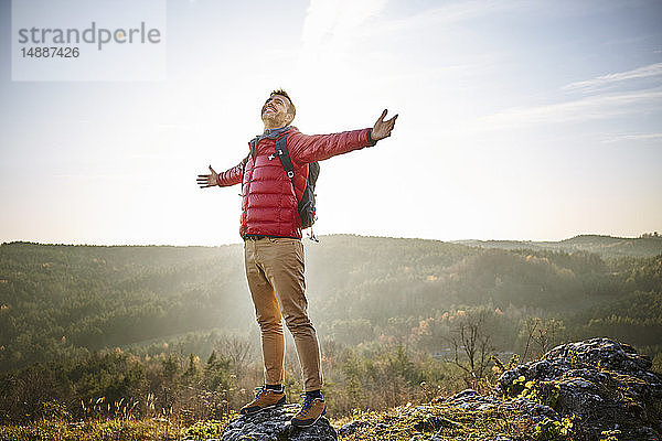 Mann auf einer Wanderung in den Bergen  der auf einem Felsen steht und die Natur genießt